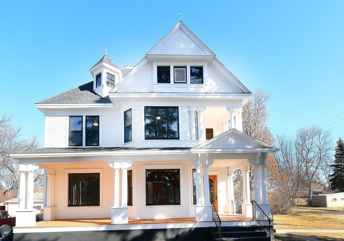 A restored white Victorian house with a wraparound porch and an orange front door